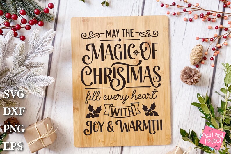 Puede incluir: Una tabla de cortar de madera con el texto "May the magic of Christmas fill every heart with joy & warmth" en letras negras. La tabla est&aacute; rodeada de vegetaci&oacute;n festiva y pi&ntilde;as.