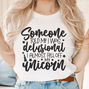 May include: A white t-shirt with black text that reads "Someone told me I was delusional I almost fell off my unicorn".