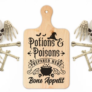Pu&ograve; includere: Un tagliere di legno con il testo "Potions & Poisons Prepared Here Bone Appetit" in lettere nere. Il tagliere &egrave; decorato con un cappello da strega, pipistrelli e un calderone. Ci sono anche diverse mani e ossa di scheletro di plastica bianca intorno al tagliere.
