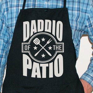 May include: Black apron with white text that reads "Daddio of the Patio" with a spatula and fork graphic.