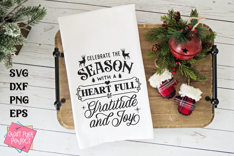 May include: White kitchen towel with black text that reads "Celebrate the Season with a Heart Full of Gratitude and Joy". The text is surrounded by a decorative border with a heart and small trees. Two deer silhouettes are above the text.