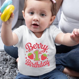 May include: A white onesie with a red and green graphic that says "Berry 1st Birthday" with two red strawberries on either side of the number one.
