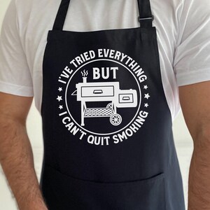 May include: Black apron with a white circle design featuring a grill and the text "I've tried everything but I can't quit smoking".