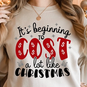 May include: A white sweatshirt with the text "It's beginning to cost a lot like Christmas" in black and red lettering. The word "cost" is in red and has dollar signs around it.