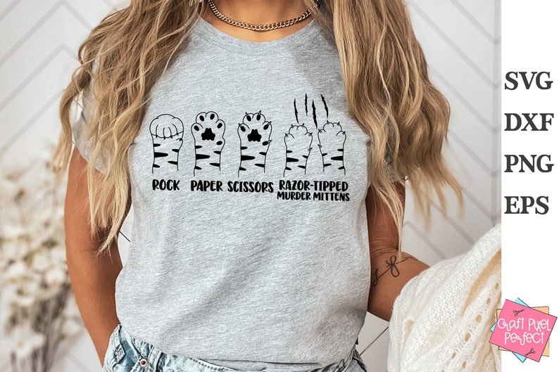 May include: A gray t-shirt with a graphic of cat paws in the shape of rock, paper, scissors, and razor-tipped murder mittens. The text "Rock Paper Scissors Razor-Tipped Murder Mittens" is printed below the graphic.
