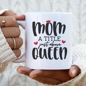 May include: White ceramic mug with a black and red design that says "Mom a title just above Queen" with a crown above the word "Mom".