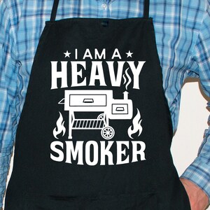 May include: Black apron with white text that reads "I am a Heavy Smoker" with a silhouette of a smoker grill.