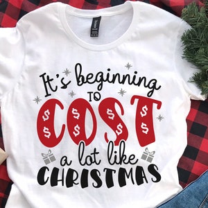 May include: White t-shirt with the text "It's beginning to cost a lot like Christmas" in black and red lettering. The word "cost" is surrounded by dollar signs.