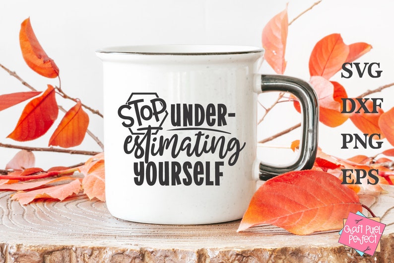 May include: White ceramic mug with a black handle. The mug features a black graphic that says "Stop Under-estimating Yourself". The mug is resting on a wooden surface with autumn leaves surrounding it.