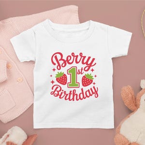 May include: White t-shirt with a red and green graphic that says "Berry 1st Birthday" with two strawberries on either side of the number one.