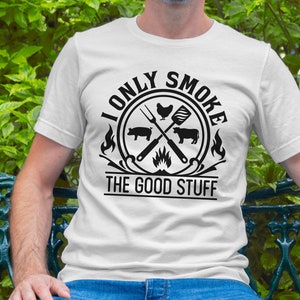 Może przedstawiać: Biały T-shirt z czarnym nadrukiem graficznym, na kt&oacute;rym widnieje napis "I only smoke the good stuff". Grafika przedstawia skrzyżowane łopatki i szczypce do grilla z kurczakiem, świnią i krową.