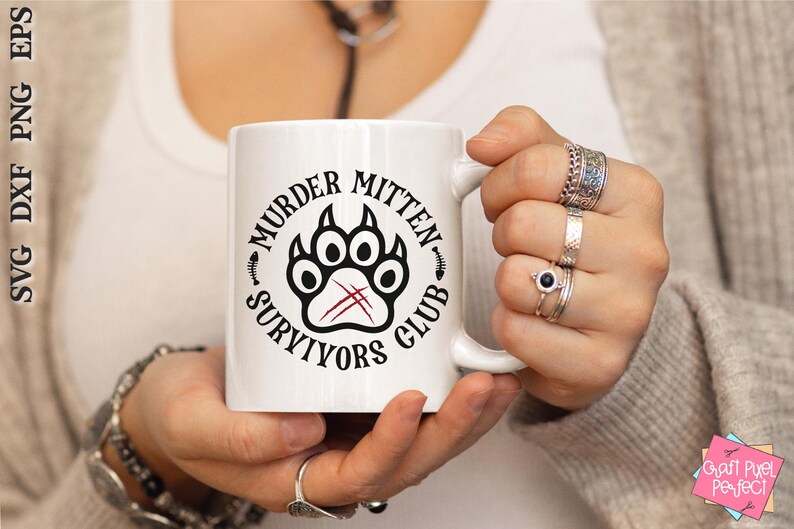 Pu&ograve; includere: Tazza in ceramica bianca con un design grafico nero e rosso. Il design presenta un'impronta di zampa con il testo "Murder Mitten Survivors Club".