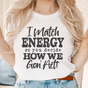 May include: White t-shirt with the text "I Match ENERGY so you decide HOW WE Gon' Act!" in a bold, dark gray font. The shirt also features the file type abbreviations SVG, DXF, PNG, and EPS. The person is wearing blue jeans.