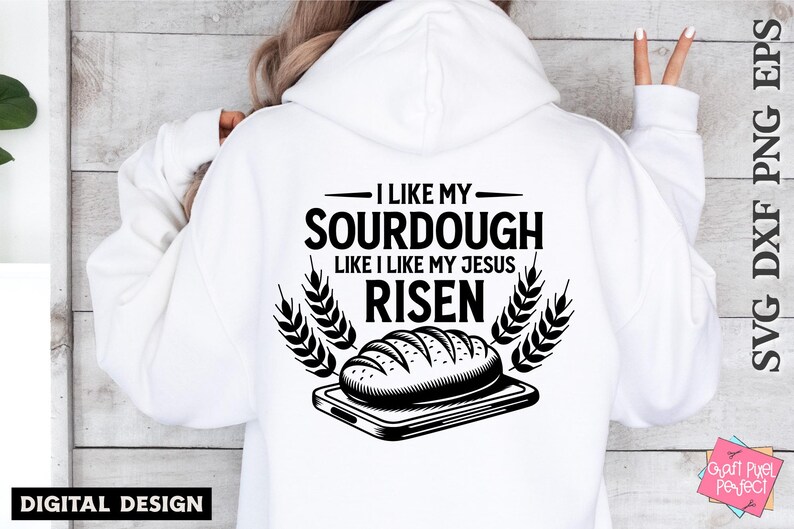 May include: A white hoodie with black text that reads "I like my sourdough like I like my Jesus risen". The text is surrounded by wheat stalks and a black and white illustration of a loaf of sourdough bread on a cutting board.