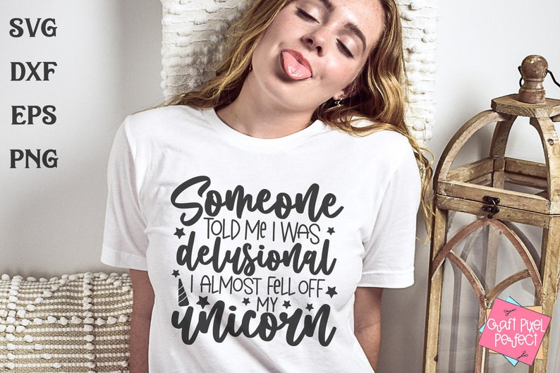 May include: A white t-shirt with black text that reads "Someone told me I was delusional I almost fell off my unicorn". The text is surrounded by small stars. The shirt is being worn by a person with long blonde hair.