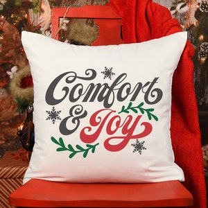May include: White throw pillow with the text "Comfort & Joy" in a festive font. The text is in gray and red with green leaves and snowflakes.