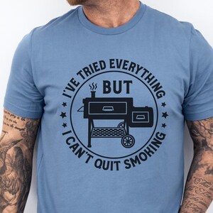May include: A blue t-shirt with a black graphic of a smoker and the text "I've tried everything but I can't quit smoking."