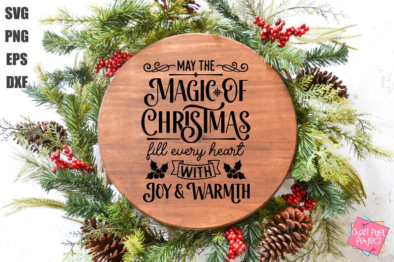 Puede incluir: Un letrero redondo de madera con el texto "May the magic of Christmas fill every heart with joy & warmth" en letras negras. El letrero est&aacute; rodeado de una guirnalda verde con bayas rojas y pi&ntilde;as.