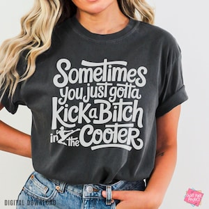 Peut inclure: T-shirt gris foncé avec l'inscription blanche : "Sometimes you just gotta Kick a Bitch in the Cooler". Le t-shirt a des manches retroussées et une coupe décontractée. Le texte est dans une police audacieuse et ludique.