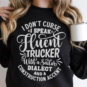 May include: Black sweatshirt with white text that reads "I don't curse - I speak fluent trucker with a sailor dialect and a construction accent".