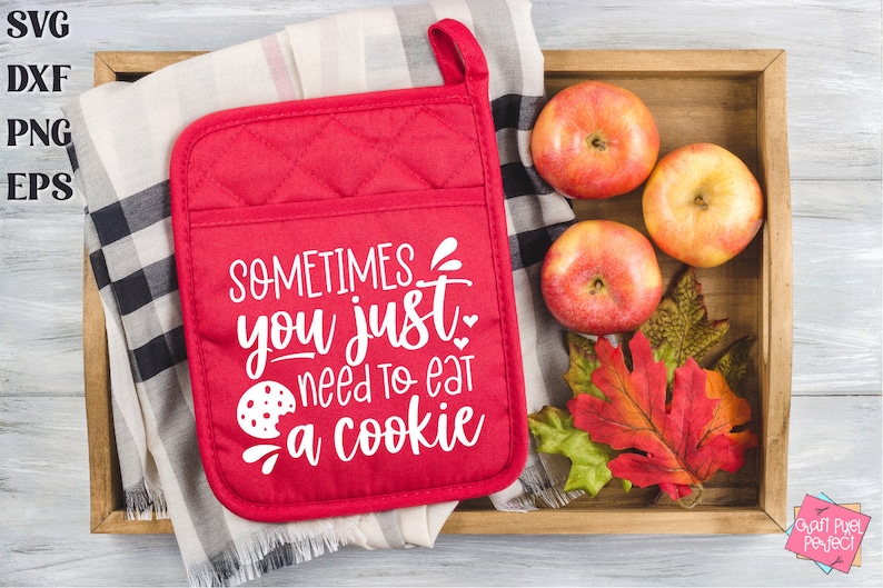 May include: Red quilted hot pad with the text "SOMETIMES you just need to eat a cookie" in white. A cookie is pictured next to the text. The hot pad is on a wooden tray with a checkered cloth, apples, and fall leaves.