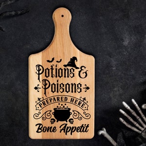 Pu&ograve; includere: Un tagliere di legno con un design in bianco e nero che dice "Pozioni e Veleni Preparati Qui. Buon appetito". Il design include un cappello da strega, un calderone e pipistrelli.