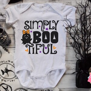 Pu&ograve; includere: Body bianco per neonato con una grafica in bianco e nero che dice "Simply Boo-tiful" con un simpatico fantasma con un fiocco.