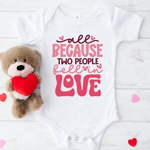 May include: White baby onesie with pink lettering that reads "all because two people fell in love".