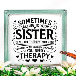 May include: A glass block with a white background and black text that reads "Sometimes talking to your sister is all the therapy you need. Sometimes after talking to your sister you need therapy." The text is surrounded by hearts and swirls.