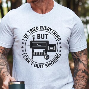 May include: A white t-shirt with a black and white graphic of a smoker and the text "I've tried everything but I can't quit smoking".