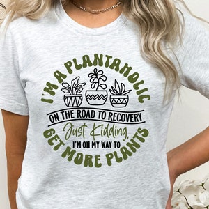May include: A white t-shirt with a green circle graphic that says "I'm a Plantaholic on the road to recovery. Just kidding, I'm on my way to get more plants."