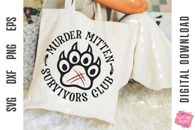 Pu&ograve; includere: Una borsa tote bianca con un design a forma di impronta di zampa nera e rossa. Il testo "Murder Mitten Survivors Club" &egrave; scritto intorno all'impronta di zampa.