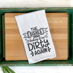 May include: A white kitchen towel with the text "THE DISHES looking at me Dirty AGAIN" in black script. The towel is on a wooden cutting board inside a distressed green tray. The image includes SVG, DXF, PNG, and EPS file type labels.