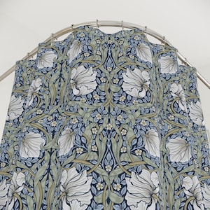 May include: A floral shower curtain with a repeating pattern of large white flowers, green leaves, and small blue and white blossoms against a dark blue background. The curtain is hanging from a curved, silver-colored shower rod.