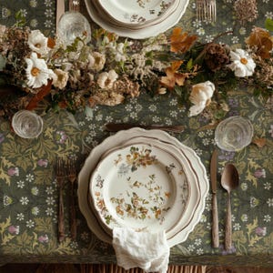 May include: A beautifully set table with floral patterned plates, silverware, and glassware. The plates have a scalloped edge and a floral design. The table is covered with a green floral tablecloth and a floral centerpiece.