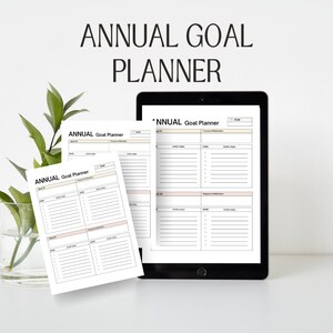 Pode incluir: Um tablet digital e duas folhas de papel impressas com o texto "ANNUAL Goal Planner" em cada uma. O planejador é projetado para ajudar as pessoas a definir e acompanhar seus objetivos.