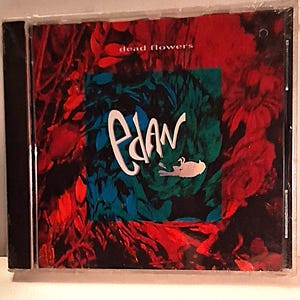 May include: A compact disc jewel case featuring cover art with a dark red and black floral background. A central teal square contains the white text Edan and the words dead flowers in small white letters at the top center.