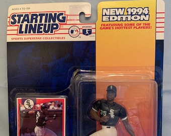Pode incluir: Uma figura de ação de plástico do jogador de beisebol Frank Thomas vestindo um uniforme preto e branco do Chicago White Sox com um taco de beisebol na mão. A figura é embalada em um blister de plástico com um verso de papelão que inclui uma foto de Frank Thomas e o texto "Starting Lineup" e "Frank Thomas".