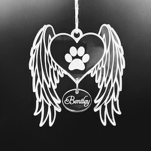 May include: White acrylic ornament shaped like a heart with wings and a paw print. The ornament has the name "Bentley" inscribed on a small circle hanging from the heart.