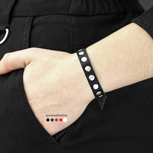 Op de afbeelding: Een zwarte leren armband met zilveren studs. De armband is verstelbaar en heeft een eenvoudig ontwerp.