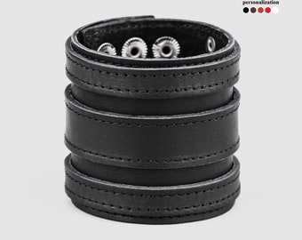 Könnte beinhalten: Schwarzes Lederarmband mit mehreren Schichten und silbernen Metallakzenten. Das Armband hat ein genähtes Design.