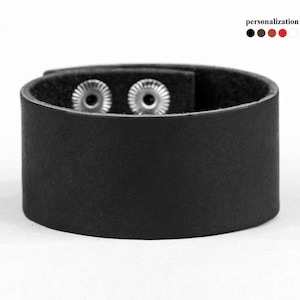 Könnte beinhalten: Ein schwarzes Lederarmband mit zwei silbernen Druckknöpfen.