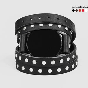 May include: Black leather watch band with silver studs. The band is wrapped around a black watch face.