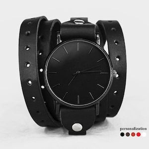 May include: Black leather wrap watch with a black face and silver hands. The watch has a minimalist design and is adjustable to fit different wrist sizes.