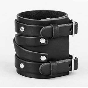 May include: Black leather bracelet with multiple straps and silver buckles. The bracelet has a layered design with multiple straps that wrap around the wrist.