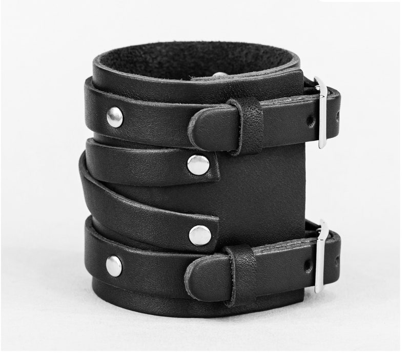 May include: Black leather bracelet with multiple straps and silver buckles. The bracelet has a layered design with multiple straps that wrap around the wrist.