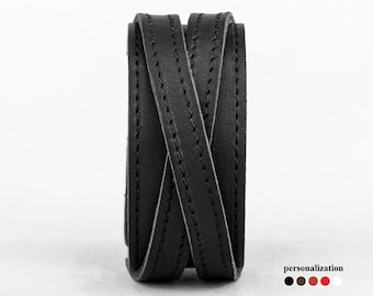 May include: Black leather bracelet with a braided design and stitching. The bracelet is rolled up and viewed from the side.