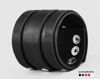 Könnte beinhalten: Schwarzes Lederarmband mit drei silbernen Druckknöpfen. Das Armband ist breit und hat eine strukturierte Oberfläche.