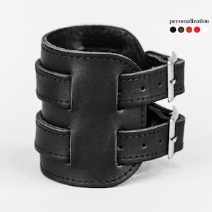 May include: Black leather cuff bracelet with two adjustable straps and silver buckles. The bracelet is made of genuine leather and has a simple, stylish design.