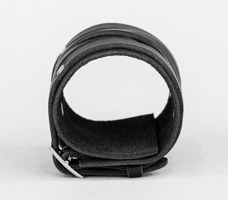 May include: A black leather cuff bracelet with a silver buckle. The bracelet is made of multiple layers of leather and has a smooth, polished finish.